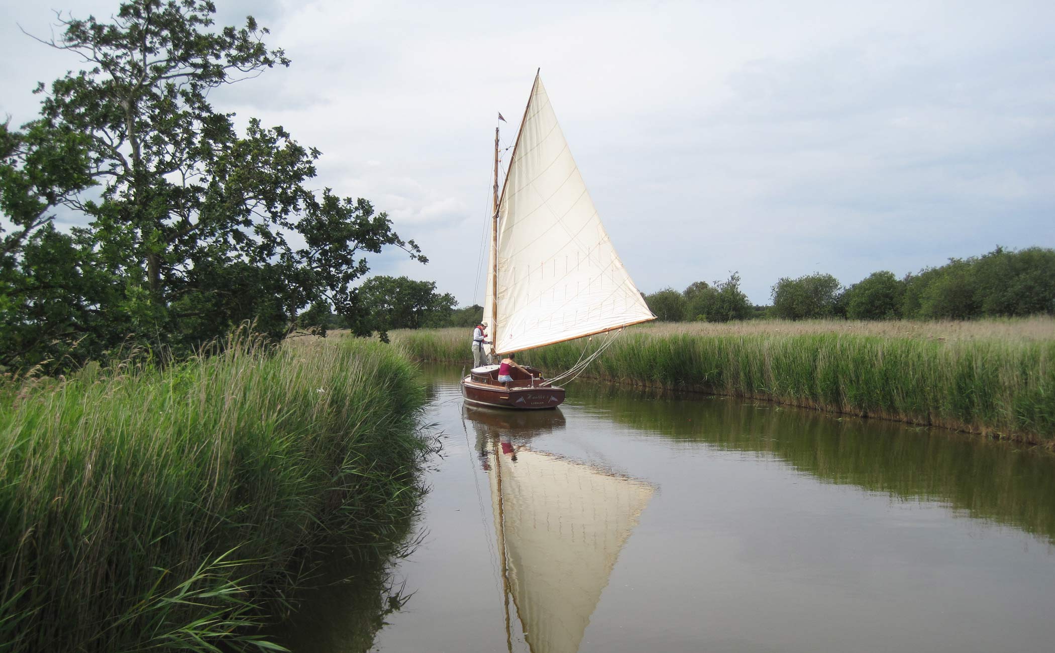 Hustler 5 meandering down a quiet river. A traditional wooden Norfolk Broads cabin yacht.